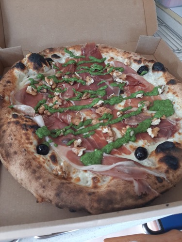 Pizza aux bords dorés, garnie et parsemée de verdure.