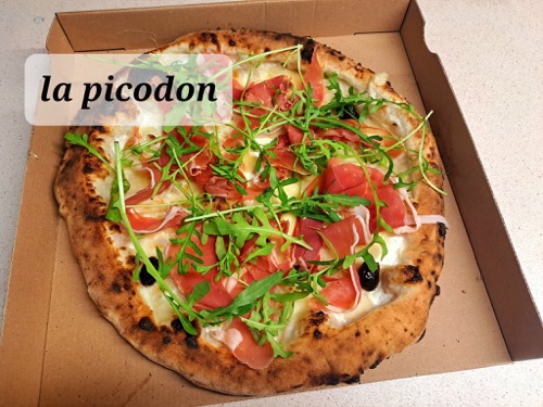 Pizza garnie de roquette, présentée dans sa boîte.
